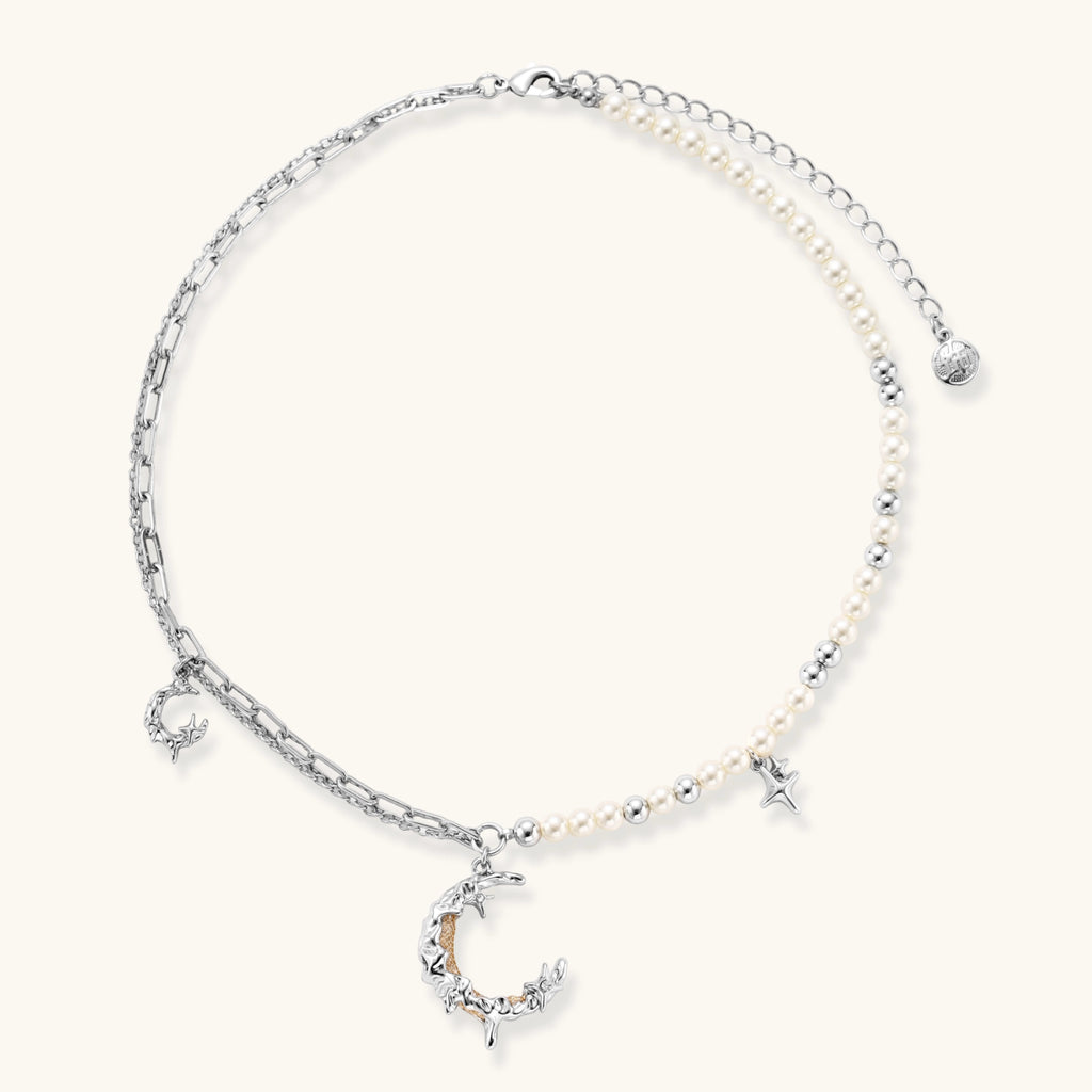 Silver-toned crescent moon pendant with star accents on pearl and chain necklace against white background.